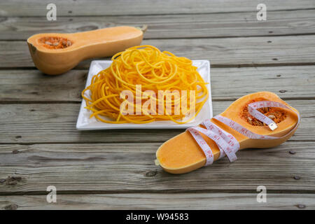 Metro a nastro avvolto intorno la zucca tagliata a metà con low carb tagliatelle in background. Giallo arancione noodle pasta - low carb, granella libera, glu Foto Stock