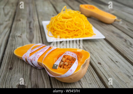 Metro a nastro avvolto intorno la zucca tagliata a metà con low carb tagliatelle in background. Giallo arancione noodle pasta - low carb, granella libera, glu Foto Stock