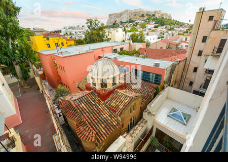 Un antica chiesa Greco Ortodossa è schiacciato tra più edifici moderni nel centro storico di Atene, Grecia, con Acropoli collina alle spalle. Foto Stock