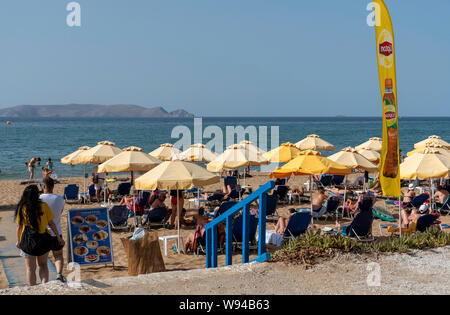 Iraklion, Creta, Grecia. Giugno 2019. Acapulco Beach si trova vicino all'aeroporto Iraklion. I turisti a prendere il sole. Dia isola disabitata in background. Foto Stock