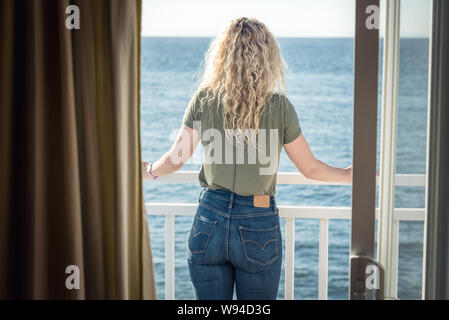 Donna bionda guardando la vista attraverso la finestra Foto Stock