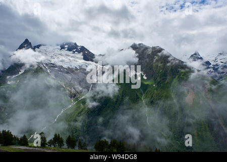 Un ghiacciaio di velatura con una verde valle di montagna nella parte inferiore. Dombay, Russia Foto Stock