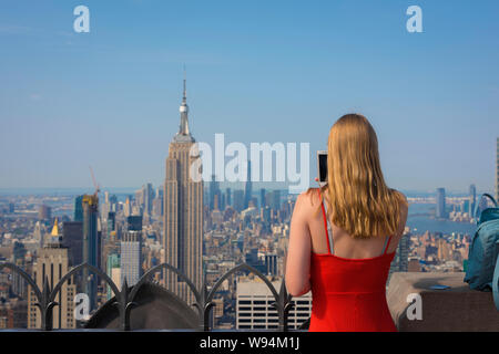 Tourist New York, vista posteriore di un turista femminile prendendo una foto del centro cittadino di Manhattan dal Rockefeller Center Observation Deck, New York City, Stati Uniti d'America Foto Stock