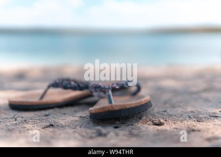 Paio di pantofole sulla sabbia in spiaggia mentre uno sfondo sfocato. Foto Stock