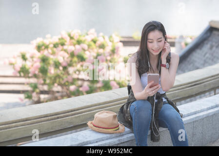 Bella asiatica solista donna turistica rilassante e piacevole ascoltare la musica sullo smartphone in città urbana del centro. Una vacanza in estate. Foto Stock