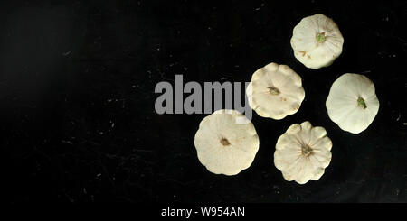 Cinque white pattypan squash su marmo nero come bordo, vista da sopra, ampia banner con spazio per testo lato sinistro Foto Stock