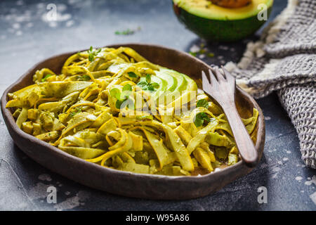 Zucchine con pasta al pesto e avocado in una piastra di scuro. Sano cibo vegan concetto. Foto Stock