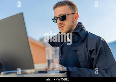Bello pensieroso elegante uomo seduto sul balcone e di lavoro sul computer portatile. Home office. Concetto di freelance. Giovane imprenditore. Foto Stock