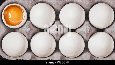 Uova bianche crude con un uovo spaccato in scatola di uova. Foto Stock