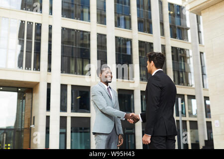 Due partner commerciali si stringono la mano e il messaggio di saluto ogni altro all aperto con edificio per uffici in background Foto Stock