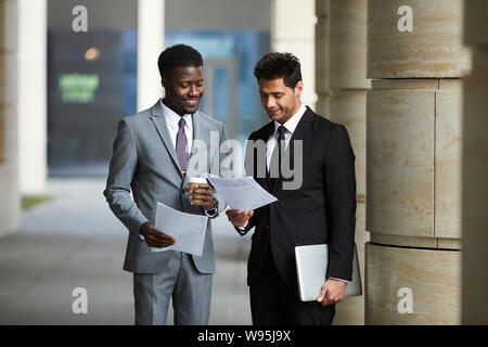 Due imprenditori in giacca lettura contratto business insieme e di bere il caffè in piedi all'aperto vicino all'edificio degli uffici Foto Stock