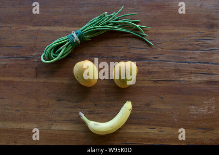 Un volto sorridente realizzata in diversi tipi di frutta e verdura su una tavola di legno Foto Stock
