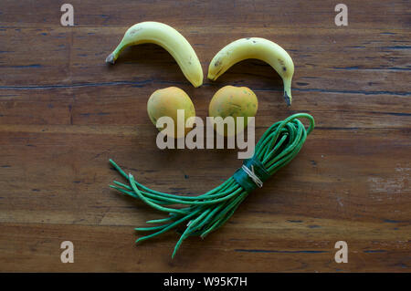 Un divertente grimace realizzata in diversi tipi di frutta e verdura su una tavola di legno Foto Stock