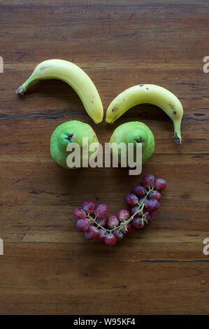 Un divertente faccia realizzata in diversi tipi di frutta su un tavolo di legno Foto Stock