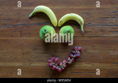 Un divertente faccia realizzata in diversi tipi di frutta su un tavolo di legno Foto Stock
