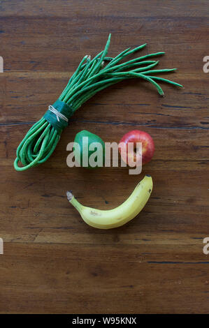 Un volto sorridente realizzata in diversi tipi di frutta e verdura su una tavola di legno Foto Stock