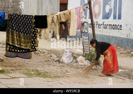 Donna in abito tradizionale lettiera di spazzamento su strada vicino l'asciugatura di biancheria, Vecchio Bazar area di Pokhara, Nepal Foto Stock