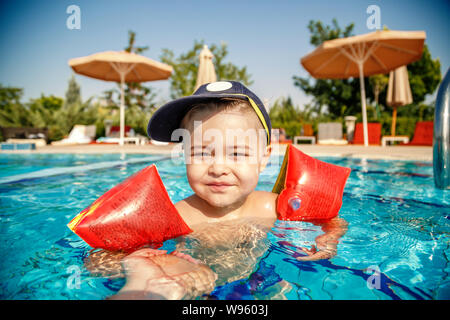 Un piccolo ragazzo impara a nuotare in piscina in estate con il sostegno di suo padre le mani Foto Stock