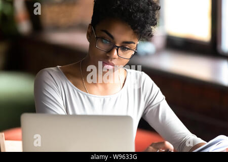Riflessivo biracial ragazza in bicchieri focalizzato lo studio sul computer portatile Foto Stock