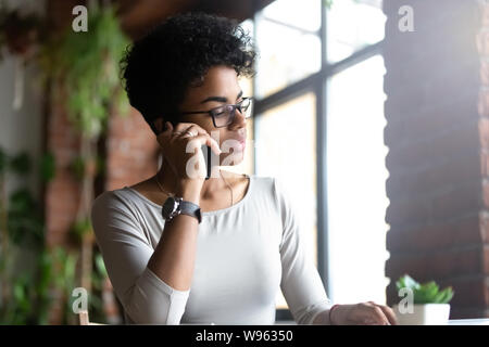 Malinconici biracial occupato femmina parlando al cellulare durante il lavoro Foto Stock