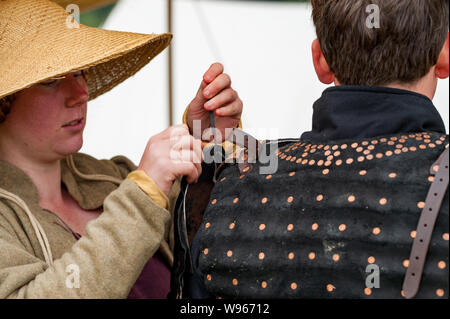 Re-enactors stadio la battaglia di Shrewsbury 1403 sul campo di battaglia di originale nel luglio 2019 donna nel cappello di paglia aiuta l uomo nel brigantino corazza Foto Stock