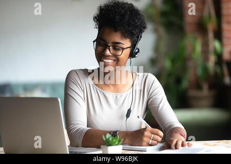 Biracial sorridente femmina in auricolari studiando rendendo note Foto Stock