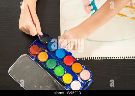 Dettaglio di un bambino con le mani in mano tenendo un pennello e pittura con acquarello su carta. Concetti di infanzia, educazione e il ritorno a scuola. Foto Stock