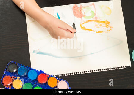 Dettaglio di un bambino con le mani in mano tenendo un pennello e pittura con acquarello su carta. Concetti di infanzia, educazione e il ritorno a scuola. Foto Stock