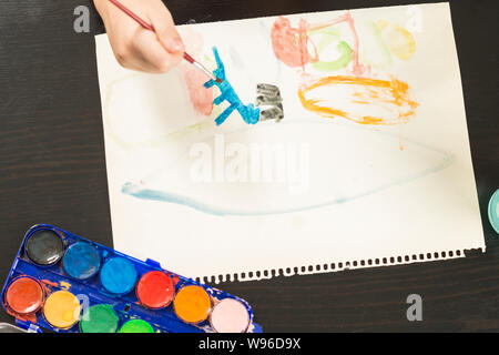 Dettaglio di un bambino con le mani in mano tenendo un pennello e pittura con acquarello su carta. Concetti di infanzia, educazione e il ritorno a scuola. Foto Stock