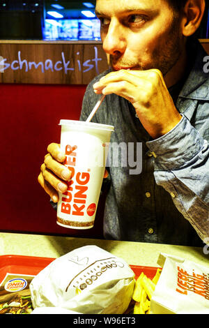 Uomo di bere attraverso una paglia dal Burger King cup Foto Stock