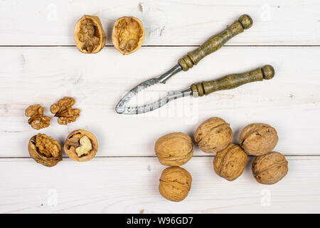 Gruppo di sacco di tutta la metà di due pezzi di mature noce marrone con il vecchio flatlay schiaccianoci in legno di colore bianco Foto Stock