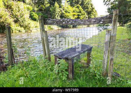 Vecchio stile in legno attraverso una staccionata in legno che danno accesso a un pubblico a piedi lungo il lato del fiume Doon, vicino a Ayr, Ayrshire, in Scozia, Regno Unito Foto Stock