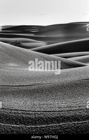Scala di grigi di alta contratto di arido deserto esanime dune di sabbia al tramonto sotto il cielo frammentato per astratta patch verticale di onde di sabbia, cadute e urti. Foto Stock