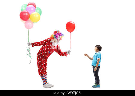 Lunghezza piena ripresa di profilo di un clown dando un palloncino per un ragazzo e tenendo un grappolo di palloncini in altro canto isolato su sfondo bianco Foto Stock