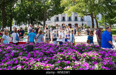 Mercato degli Agricoltori, Madison, WI, Stati Uniti d'America. Aug 2018. Persone che camminano verso il mercato dal lussureggiante giardino fiorito presso lo State Capitol. Foto Stock