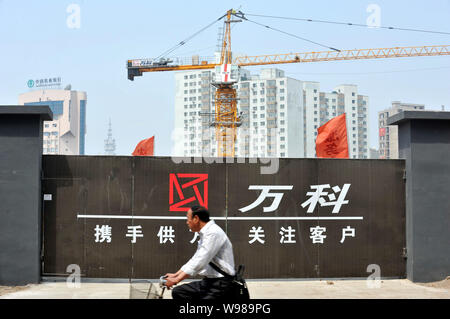 --FILE--un ciclista cinese cavalca la sua moto passato il cantiere per la costruzione di un progetto residenziale sviluppato da Vanke in Shenyang city, nordest Chinas Lia Foto Stock