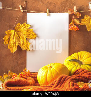 Vuoto foglio di carta bianco foglie secche appesi clothespins con zucca sciarpa sfondo marrone. Cartolina di autunno Foto Stock