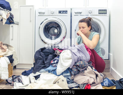 Stanco donna infelice casalinga in una sala lavanderia vicino alla macchina di lavaggio Foto Stock