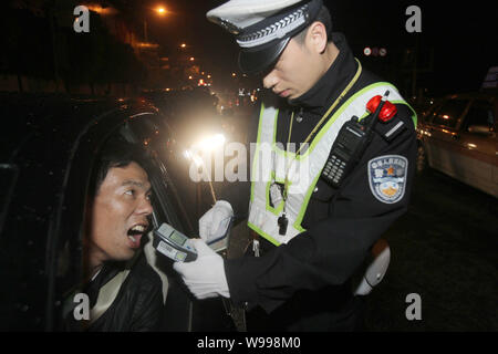 Un Cinese funzionario di polizia usa un rivelatore per misurare il livello di alcol nel sangue di un operatore durante la guida in stato di ebbrezza la prova in città di Nantong, Oriente Cina Foto Stock