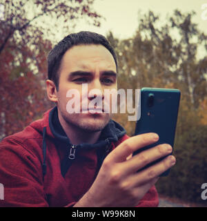 Guy utilizza lo smartphone dispositivo all'aperto, outdoor Ritratto di giovane uomo allegro texting un messaggio SMS a reti sociali, il concetto di tecnologia, dispiacere Foto Stock