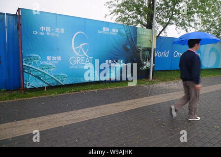 Un uomo cinese passeggiate passato manifesti pubblicitari dei mondi più alto ruota panoramica Ferris presso il suo cantiere in cui la costruzione è stata interrotta al Parco Chaoyang Foto Stock