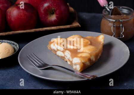 Un pezzo di torta di mela su lastra grigia in autunno impostazione con mele e cannella e oggetti in legno Foto Stock