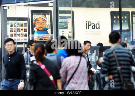 --FILE--Cinesi locali residenti a piedi passato un Apple Store in cui i clienti sono shopping nella parte anteriore di un annuncio pubblicitario per l'iPad Apple a Pechino, C Foto Stock