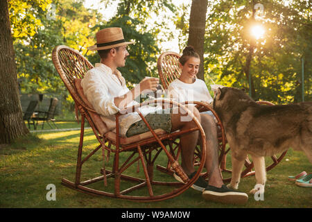 Coppia felice di mangiare e di bere birre a cena con barbecue sul tramonto. Avente pasto insieme all'aperto in una radura della foresta. Celebrando e rilassante. Estate stile di vita, cibo, famiglia, rispetto del concetto. Foto Stock