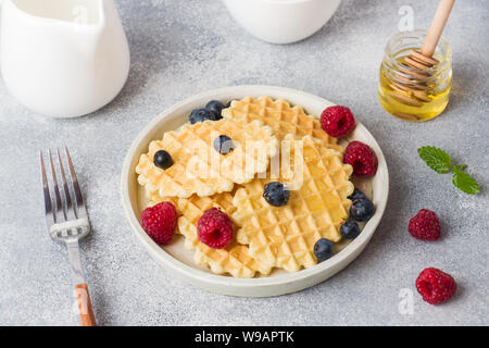 Waffle ondulato i cookie con lamponi freschi e mirtilli su un sfondo di calcestruzzo. Spazio di copia Foto Stock