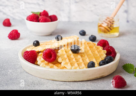 Waffle ondulato i cookie con lamponi freschi e mirtilli su un sfondo di calcestruzzo. Spazio di copia Foto Stock