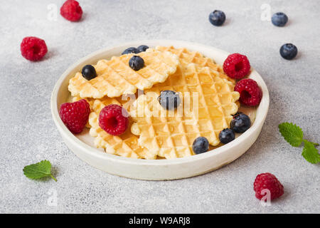 Waffle ondulato i cookie con lamponi freschi e mirtilli su un sfondo di calcestruzzo. Spazio di copia Foto Stock