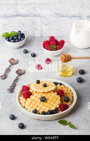 Waffle ondulato i cookie con lamponi freschi e mirtilli su un sfondo di calcestruzzo. Spazio di copia Foto Stock