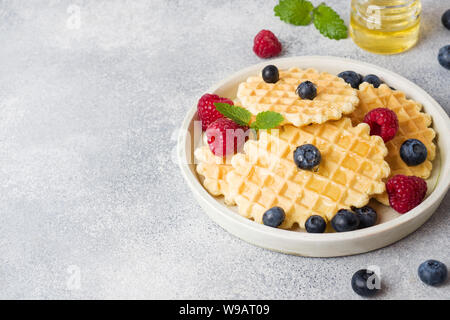 Waffle ondulato i cookie con lamponi freschi e mirtilli su un sfondo di calcestruzzo. Spazio di copia Foto Stock