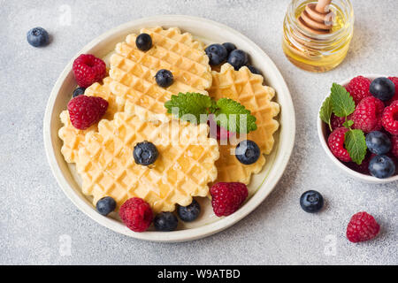 Waffle ondulato i cookie con lamponi freschi e mirtilli su un sfondo di calcestruzzo. Spazio di copia Foto Stock